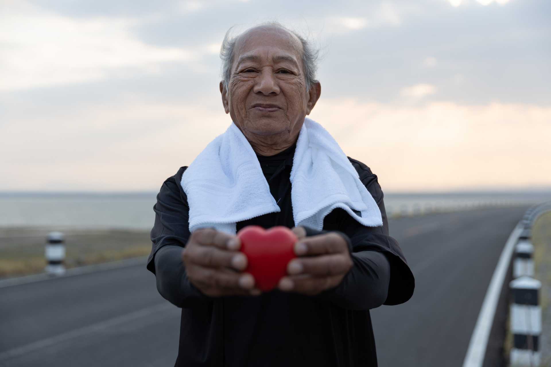 A senior man on a run, holding a red heart shape.